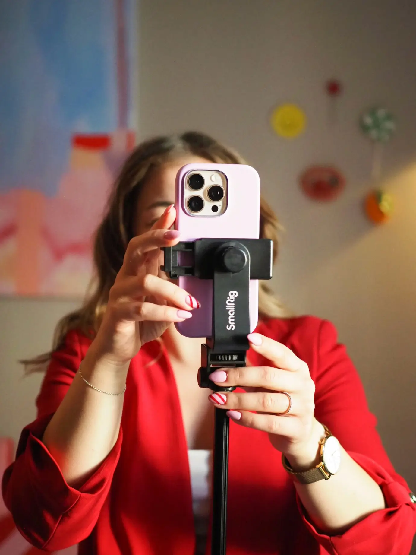 A person in a red blazer places a lilac phone into a tripod mount, getting ready to shoot a short-form video.